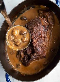 a pot filled with meat and gravy on top of a stove next to a spoon