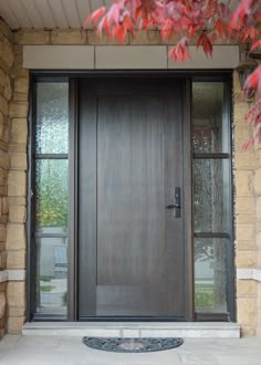 the front door to a home with glass doors and brick pillars, surrounded by red leaves