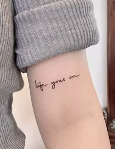 a woman's arm with the words life goes on written in cursive font