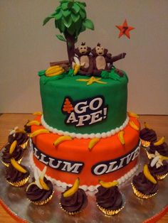 a three tiered cake decorated with monkeys and palm trees on the top, surrounded by cupcakes