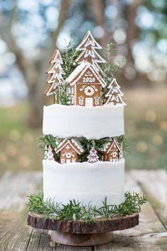 a three tiered cake decorated with gingerbread houses and fir trees is on a wooden table