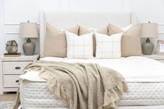 a white bed with pillows and blankets on top of it in front of two nightstands