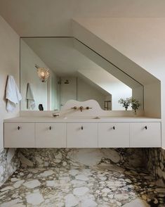 a bathroom with marble flooring and white walls, along with a large mirror on the wall