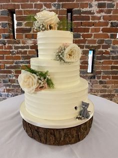 a three tiered cake with flowers on the top is sitting on a table in front of a brick wall