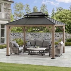 a gazebo sitting on top of a patio next to a stone wall and grass