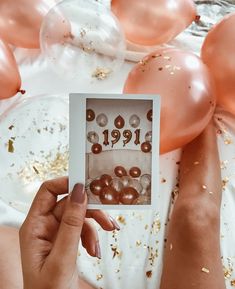 a person holding up an old photo with balloons and confetti in the background