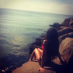 a woman sitting on top of a rock next to the ocean