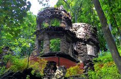 an old building sitting in the middle of a forest filled with trees and bushes on top of a lush green hillside