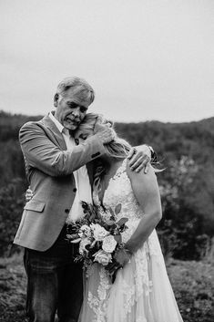 a man and woman standing next to each other in front of a field with trees