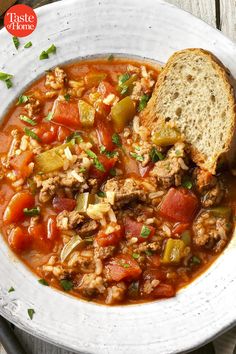 a white bowl filled with meat and vegetable soup on top of a wooden table next to a piece of bread