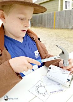 a young boy sitting at a table with a hammer and some construction paper on it