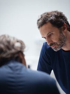 a man in a blue shirt is looking at another man's face while he sits down