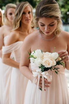 two bridesmaids in white dresses are looking at their bouquets