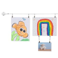 two children's drawings hanging on a clothes line with a teddy bear next to them