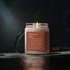 a candle sitting on top of a wooden table next to a black mug with the words difference maker written on it