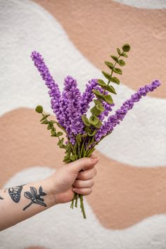 a person's arm holding a bouquet of purple flowers in front of a wall