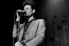 a black and white photo of a man in a suit on stage singing into a microphone