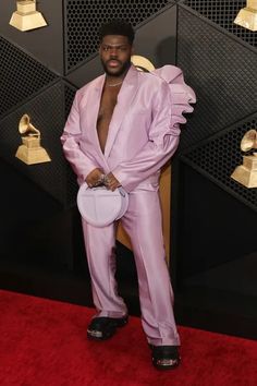 a man in a pink suit and black shoes standing on a red carpet with gold bells