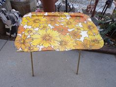 an orange and yellow flowered tray sitting on top of a metal stand next to potted plants