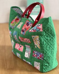 a green handbag with red handles sitting on top of a wooden table