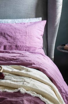 a bed with purple sheets and pillows on top of it next to a nightstand table