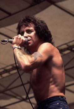 a shirtless man holding a microphone up to his ear while standing on stage at a music festival