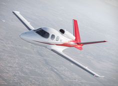 a small white and red airplane flying in the sky above land area with buildings below