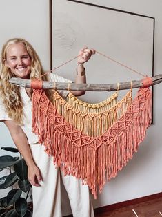 a woman is holding up a piece of wood with tassels hanging from it