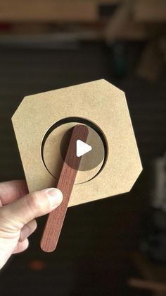 a person holding a piece of cardboard with a wooden stick sticking out of it's center