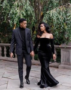 a man and woman dressed in formal wear walking down a sidewalk holding hands with each other