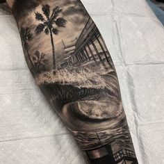 a man's arm with a black and white painting on it that has a palm tree in the water