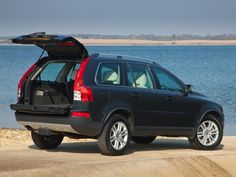 the back end of a black volvo car with its trunk open and water in the background