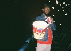 a man standing in front of a movie theater holding a bucket with popcorn on it