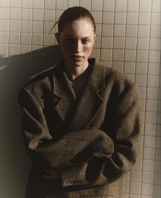 a woman standing in front of a white tiled wall with her arms crossed and looking at the camera