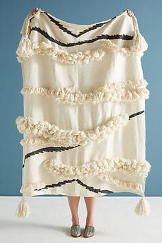 a woman is holding up a blanket with ruffles and tassels on it