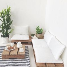 a living room filled with white furniture and potted plants on top of wooden tables