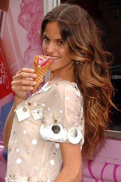 a woman eating an ice cream cone in front of a pink wall with coca cola advertisement