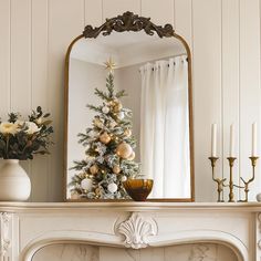 a decorated christmas tree sitting on top of a mantle next to a mirror and candles