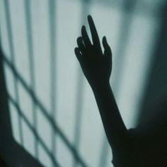 the shadow of a person's hand in front of a window with bars on it