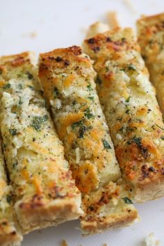 four pieces of bread with cheese and herbs on it sitting on a white surface next to other food items