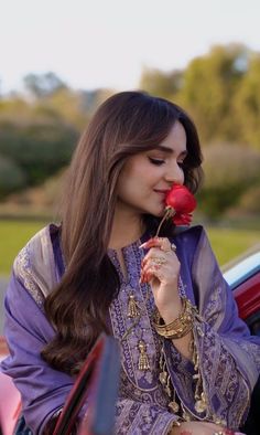 a woman is holding a rose in her hand and looking at the car door window