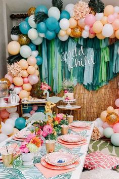 a table set up for a party with balloons, plates and place settings on it