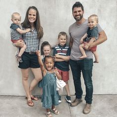 a group of people standing next to each other near a wall with two children and one adult