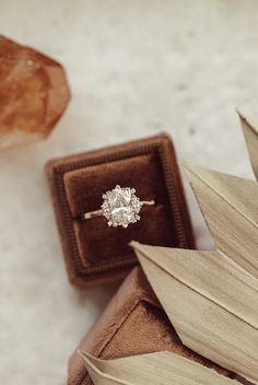 an engagement ring sitting on top of a wooden box next to a rock and leaf