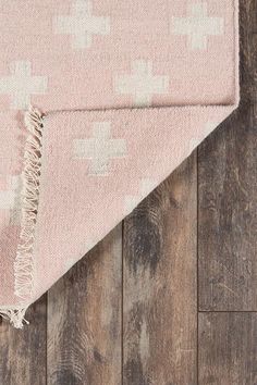 a pink and white rug on top of a wooden floor with a wood flooring pattern