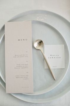 a white plate topped with a menu and a silver spoon next to a card on top of it