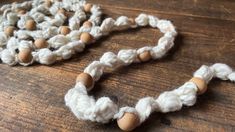 a white crocheted necklace with wooden beads on a table next to a piece of wood