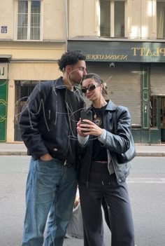 two people standing next to each other in front of a building with a street sign