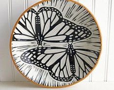 a black and white plate with a butterfly design on the front, hanging from a hook