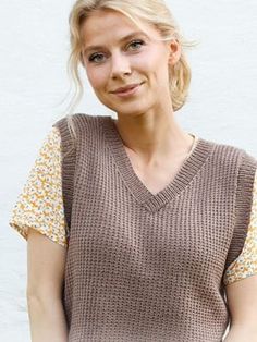 a woman with blonde hair wearing a brown knitted vest and smiling at the camera